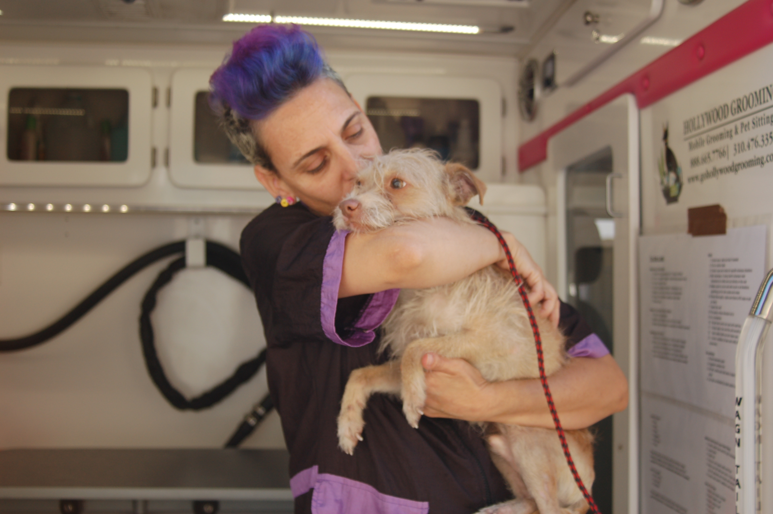 Yael hugs a dog at a Grooming Station at a community event.