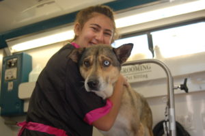 Dog Groomer Danielle hugs a dog at a Grooming Station.