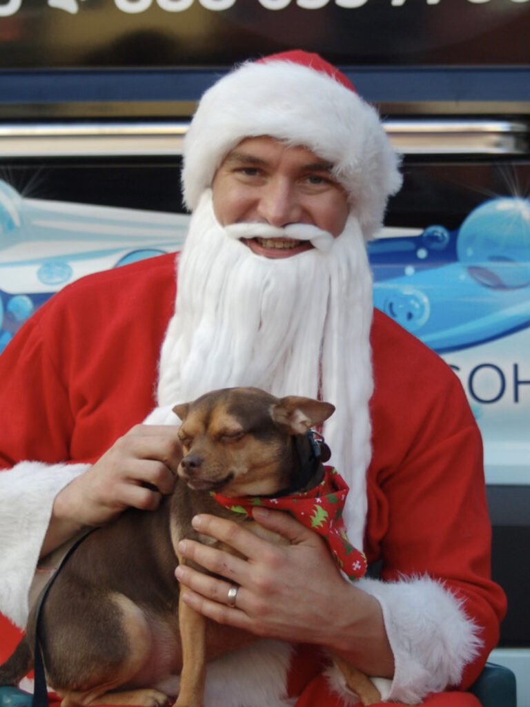 Santa with an adorable dog wearing a Christmas bow.